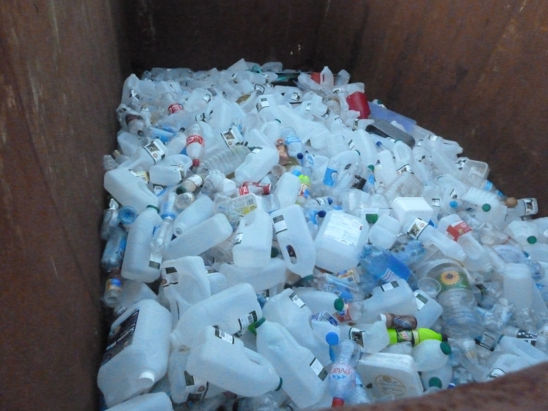 A large pile of empty plastic milk containers inside a rusted metal container.