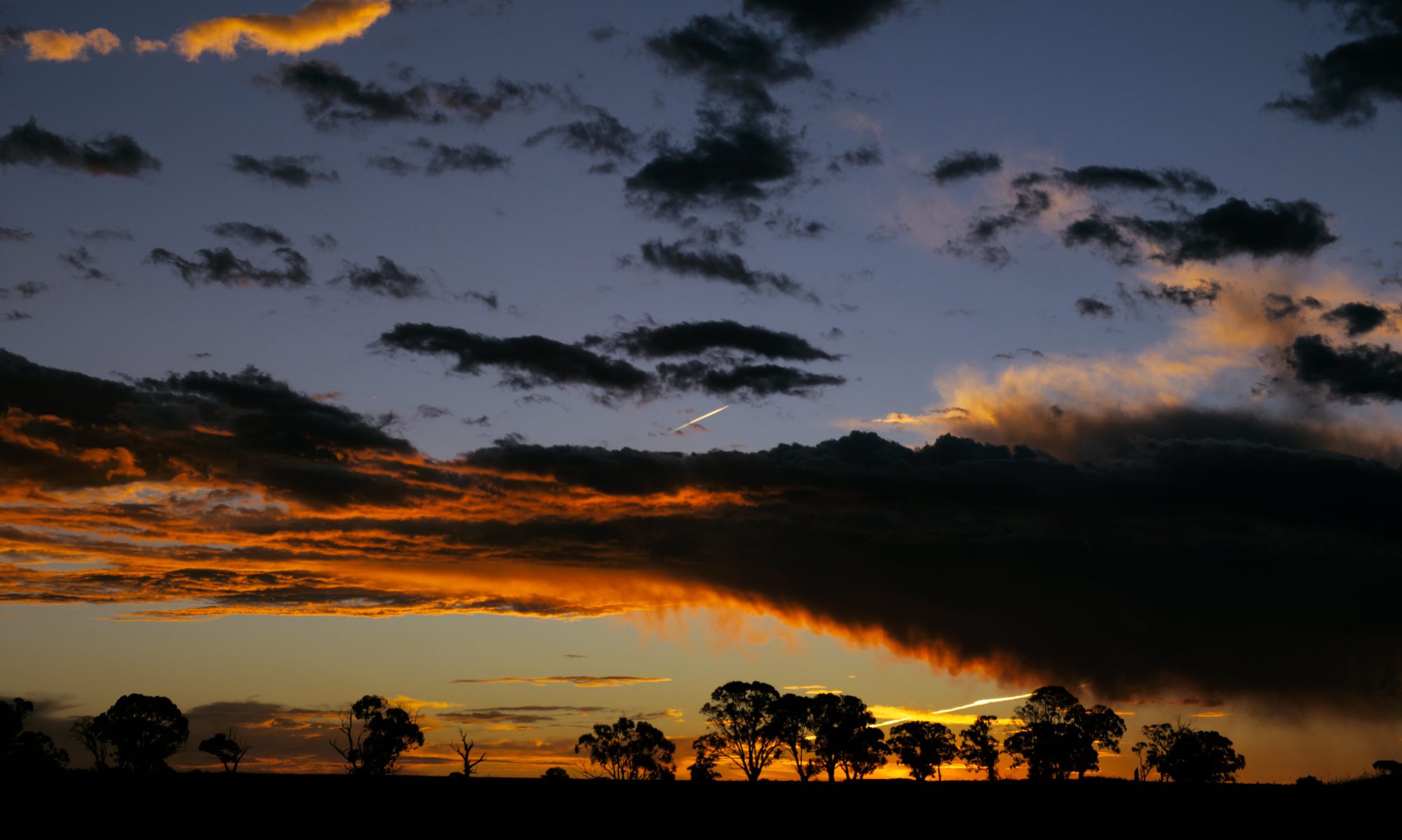 A band of storm clouds lit red and orange by the setting sun.