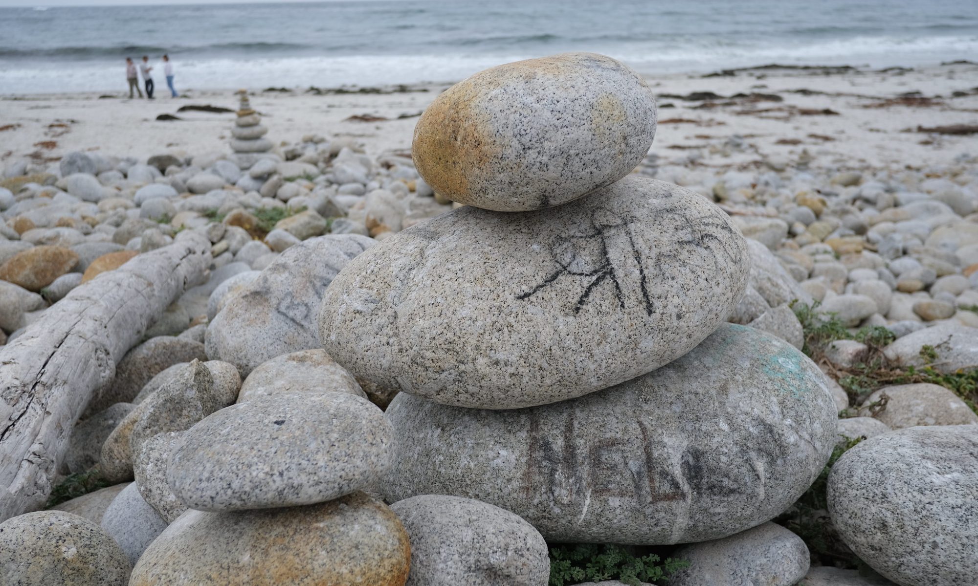 A pile of smooth stones, some featuring writing, on a beach.